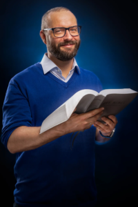 Ein bärtiger Mann in blauem Pullover hält ein Buch