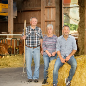 Stefan Lehner und seine Eltern sitzen auf Strohballen in Stall, Hintergrund Kühe